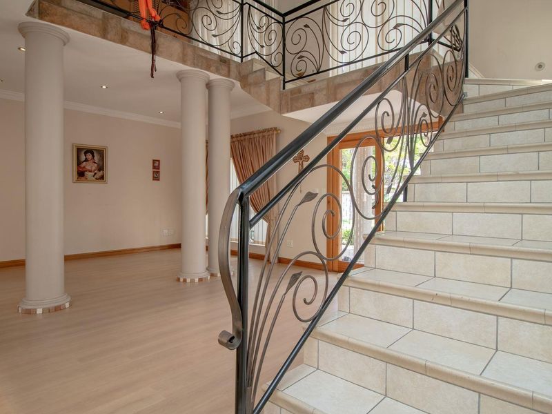 Spacious entrance hall featuring a grand tiled staircase with decorative wrought iron balustrades, structural columns, and neutral laminate flooring.