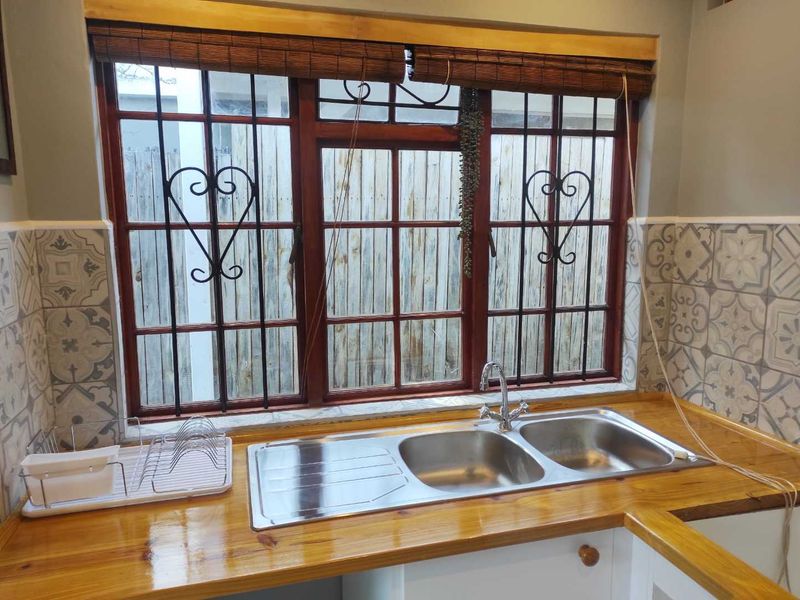 A clean kitchen area featuring a double bowl stainless steel sink, polished wooden countertops, and decorative patterned wall tiles under a timber-framed window.