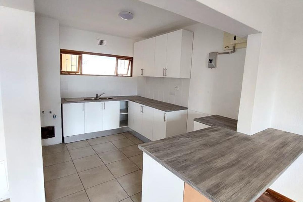 A functional kitchen featuring white cabinetry, wood-look laminate countertops, a breakfast bar, and a mix of tiled and parquet flooring.