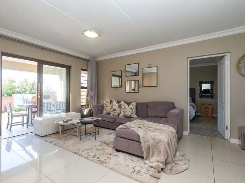 A well-maintained living room featuring large format floor tiles, coved ceilings, and a sliding glass door providing access to an outdoor patio area.