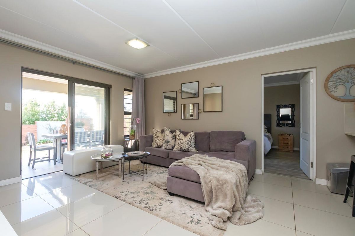 A well-maintained living room featuring large format floor tiles, coved ceilings, and a sliding glass door providing access to an outdoor patio area.