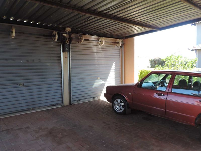 A covered double garage area featuring corrugated metal roofing, roller shutter doors, and paved flooring.