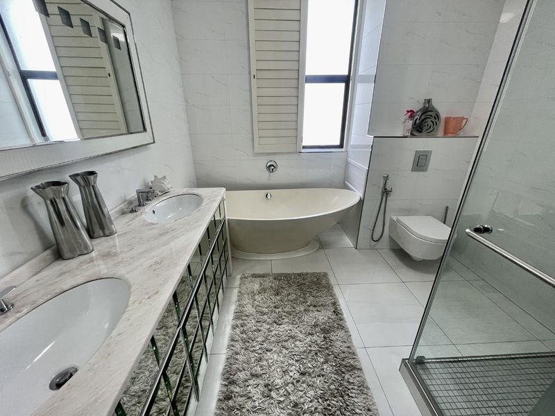 Modern bathroom featuring a double vanity with marble countertop, a sleek freestanding bathtub, wall-mounted toilet, and a separate glass-enclosed shower.