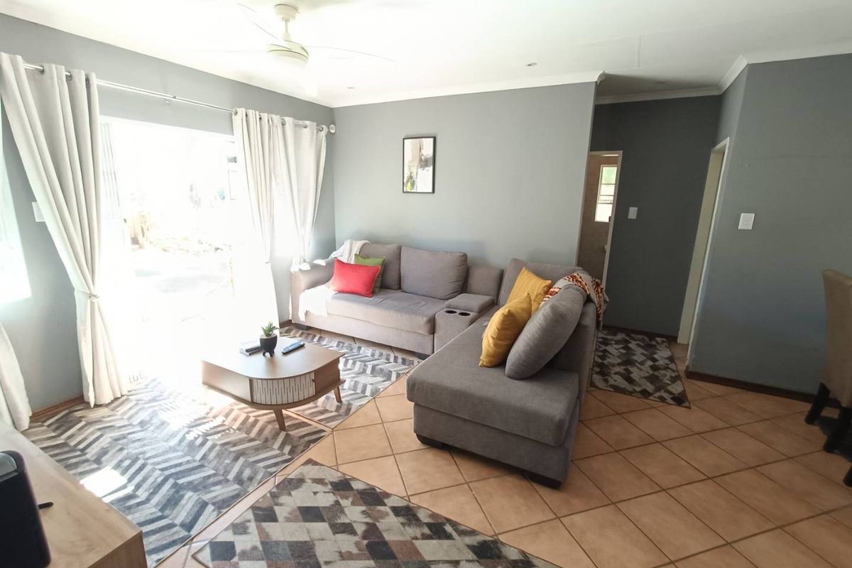 A spacious living room featuring tiled flooring, a ceiling fan, and large sliding glass doors that provide direct access to the outdoor area.