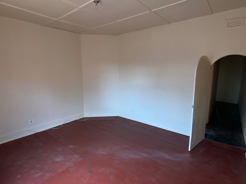An empty living room featuring original timber flooring, an arched doorway, and a tiled ceiling, offering a blank canvas for renovation.