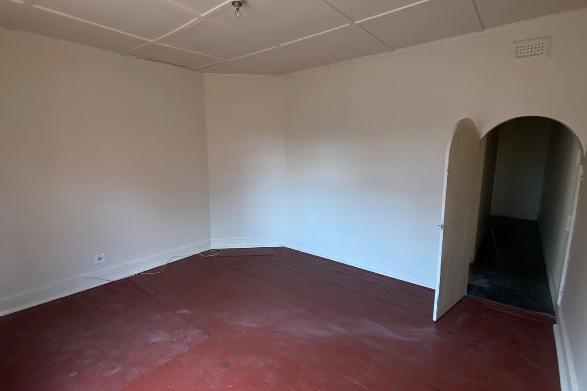 An empty living room featuring original timber flooring, an arched doorway, and a tiled ceiling, offering a blank canvas for renovation.