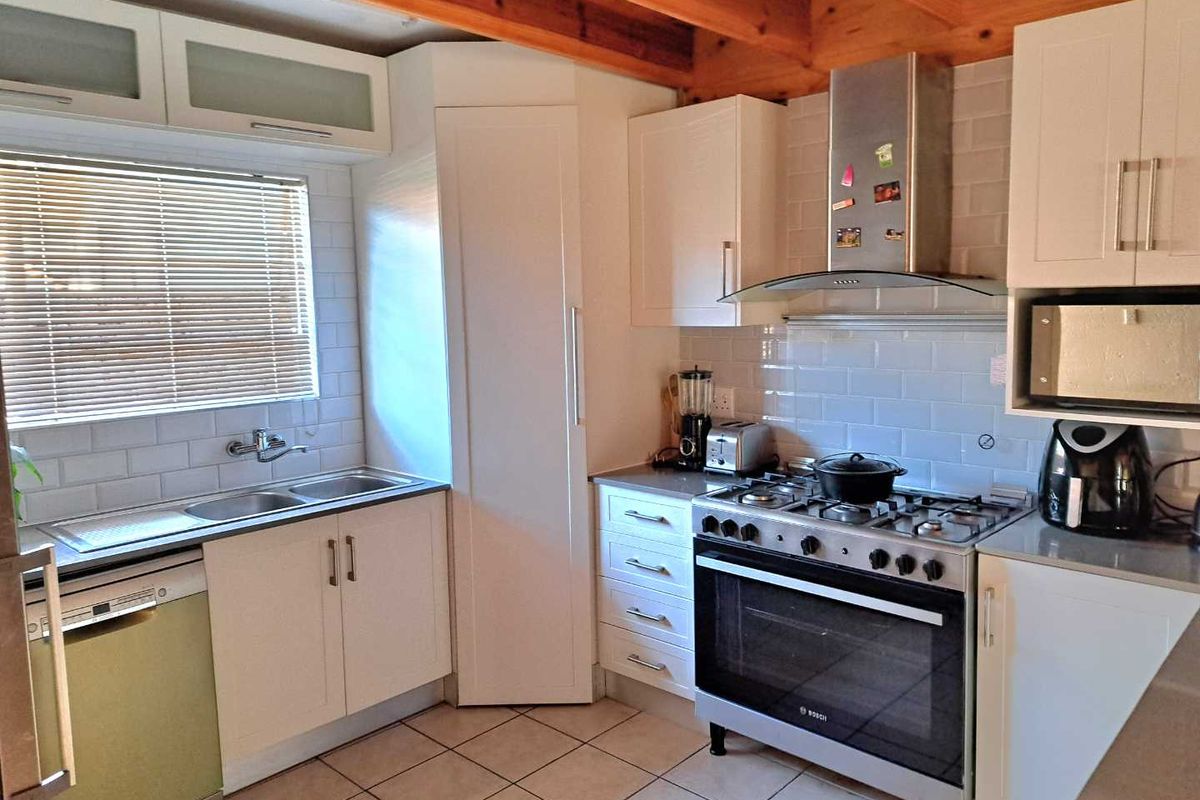 A functional kitchen featuring white cabinetry, subway tile backsplash, stainless steel gas stove with extractor fan, and tiled flooring with exposed timber ceiling beams.