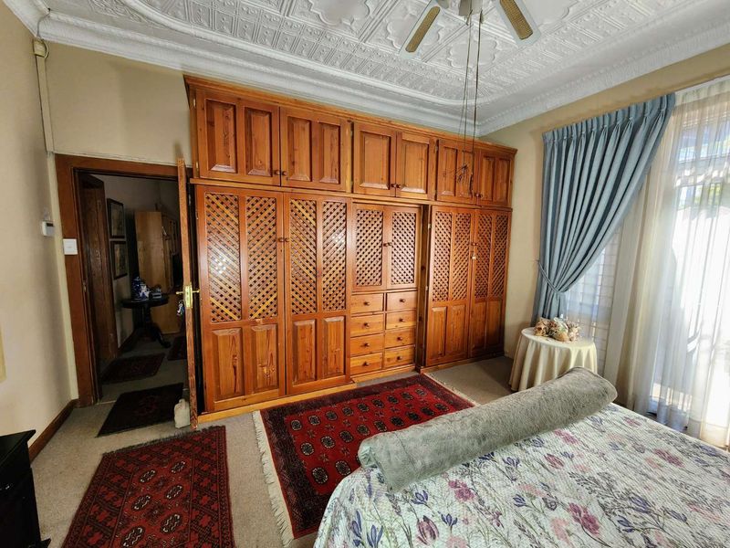 A bedroom featuring a large built-in wooden wardrobe, an ornate pressed metal ceiling, and a ceiling fan.
