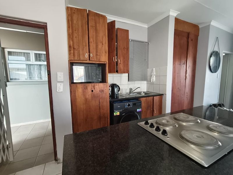 Compact kitchen featuring dark granite countertops, an integrated electric hob, and wooden cabinetry with built-in microwave space.