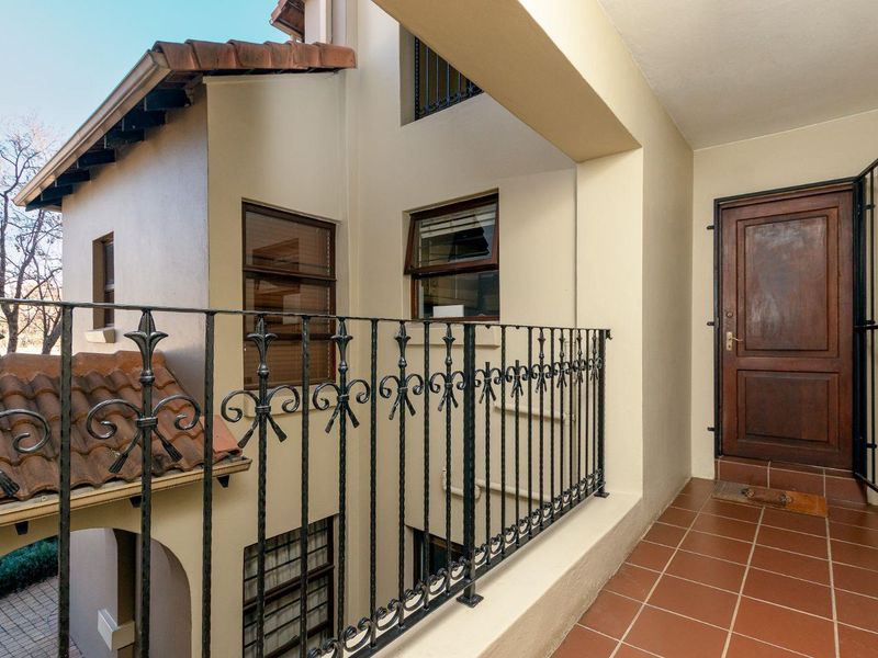 An elevated balcony entrance featuring terracotta tiling, a wrought iron balustrade, and a solid wooden front door with a security gate.