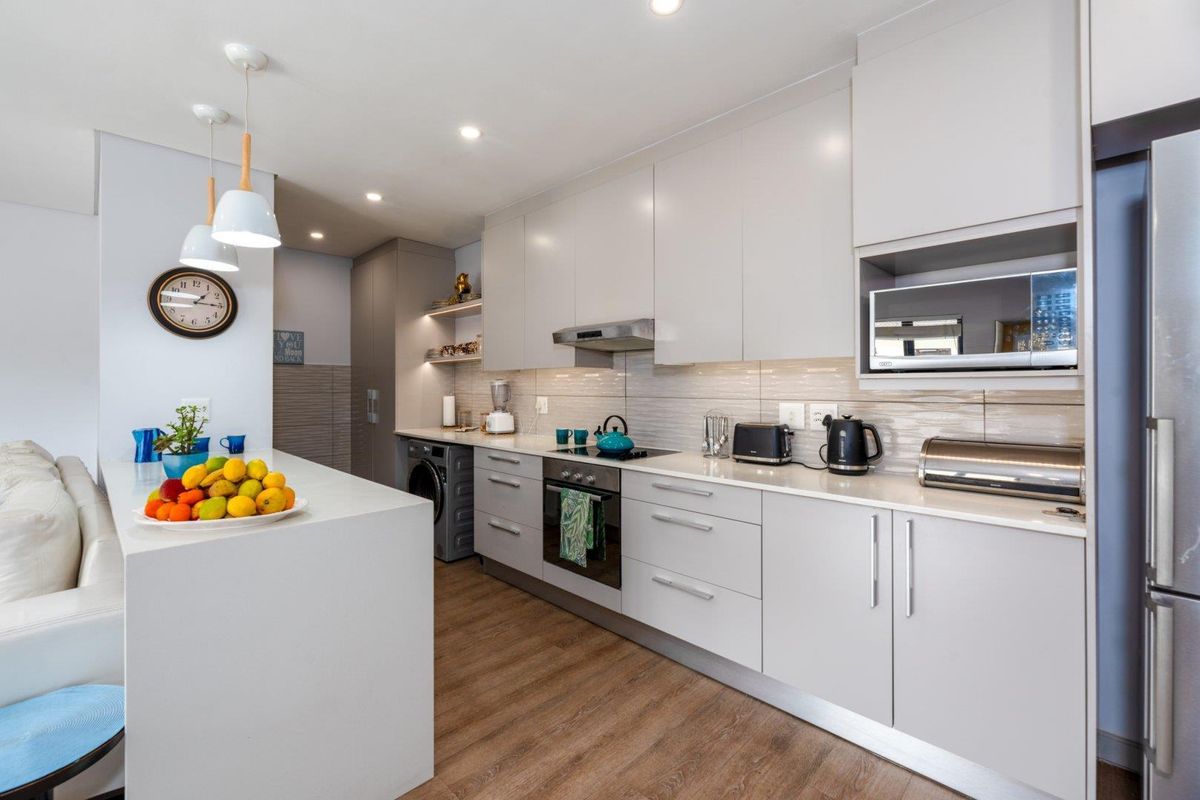 Modern kitchen featuring sleek cabinetry, integrated appliances, built-in oven, hob, extractor fan, and a functional breakfast island with pendant lighting.