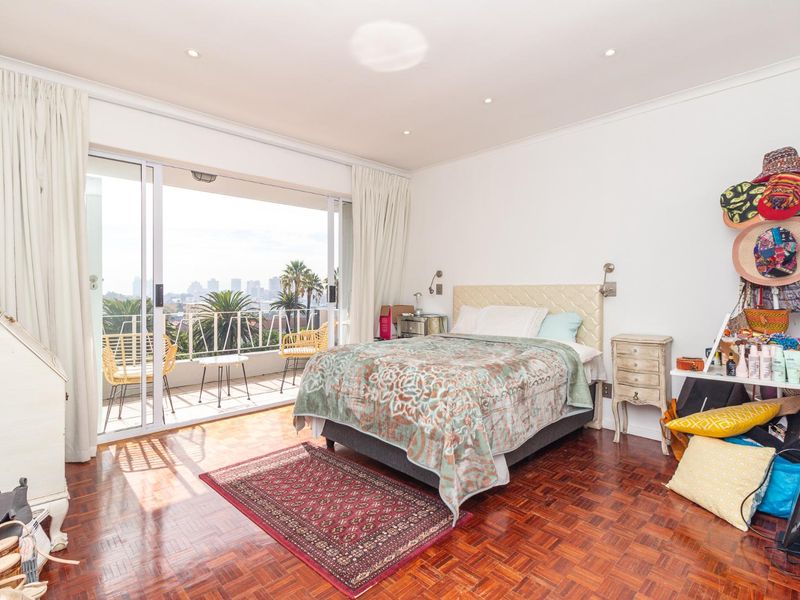 Spacious bedroom featuring classic parquet flooring and large sliding glass doors that open onto a private balcony with city views.