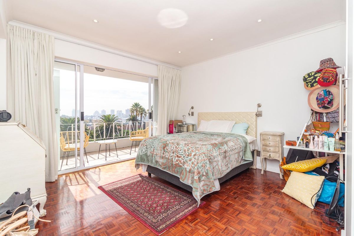Spacious bedroom featuring classic parquet flooring and large sliding glass doors that open onto a private balcony with city views.