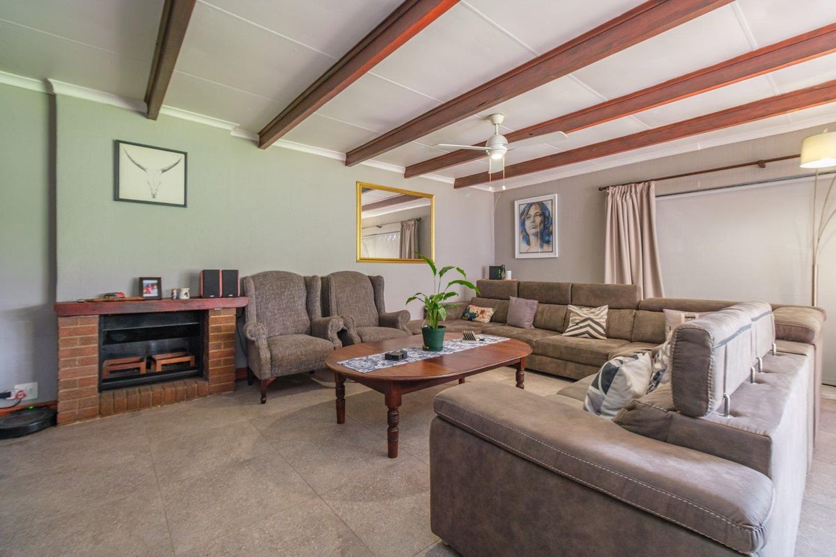 Spacious living room featuring exposed timber ceiling beams, a brick fireplace, and neutral tiled flooring, offering a comfortable and inviting atmosphere.
