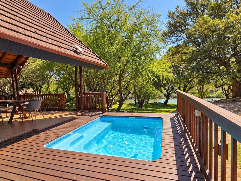 Outdoor entertainment area featuring a plunge pool set into timber decking, covered by a thatched roof, overlooking a scenic garden and river view.
