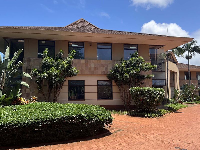 A well-maintained two-story office building featuring a tiled facade, hipped roof, and extensive paved driveway area.