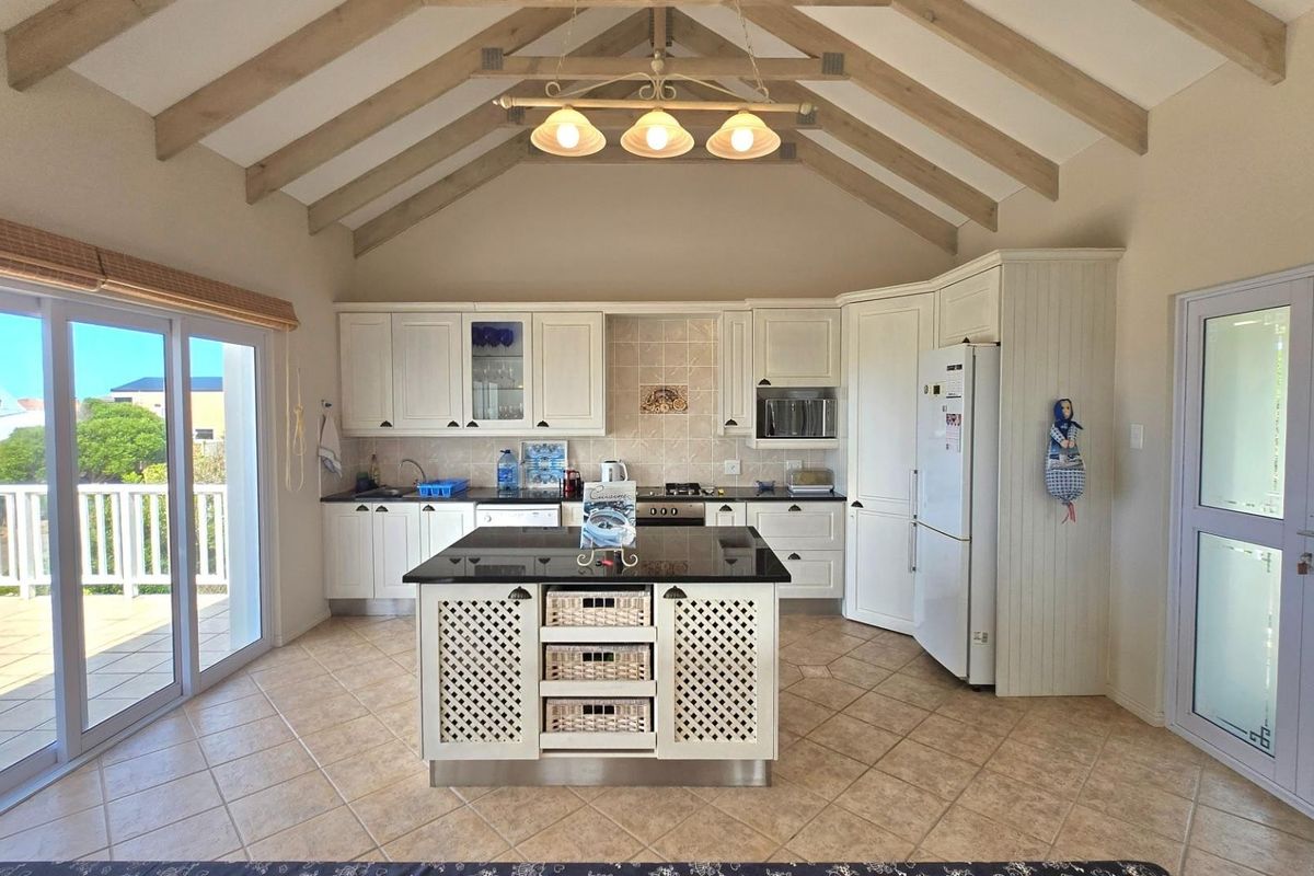 Spacious kitchen featuring a vaulted ceiling with exposed beams, a central island with granite countertops, and direct access to an outdoor patio area.