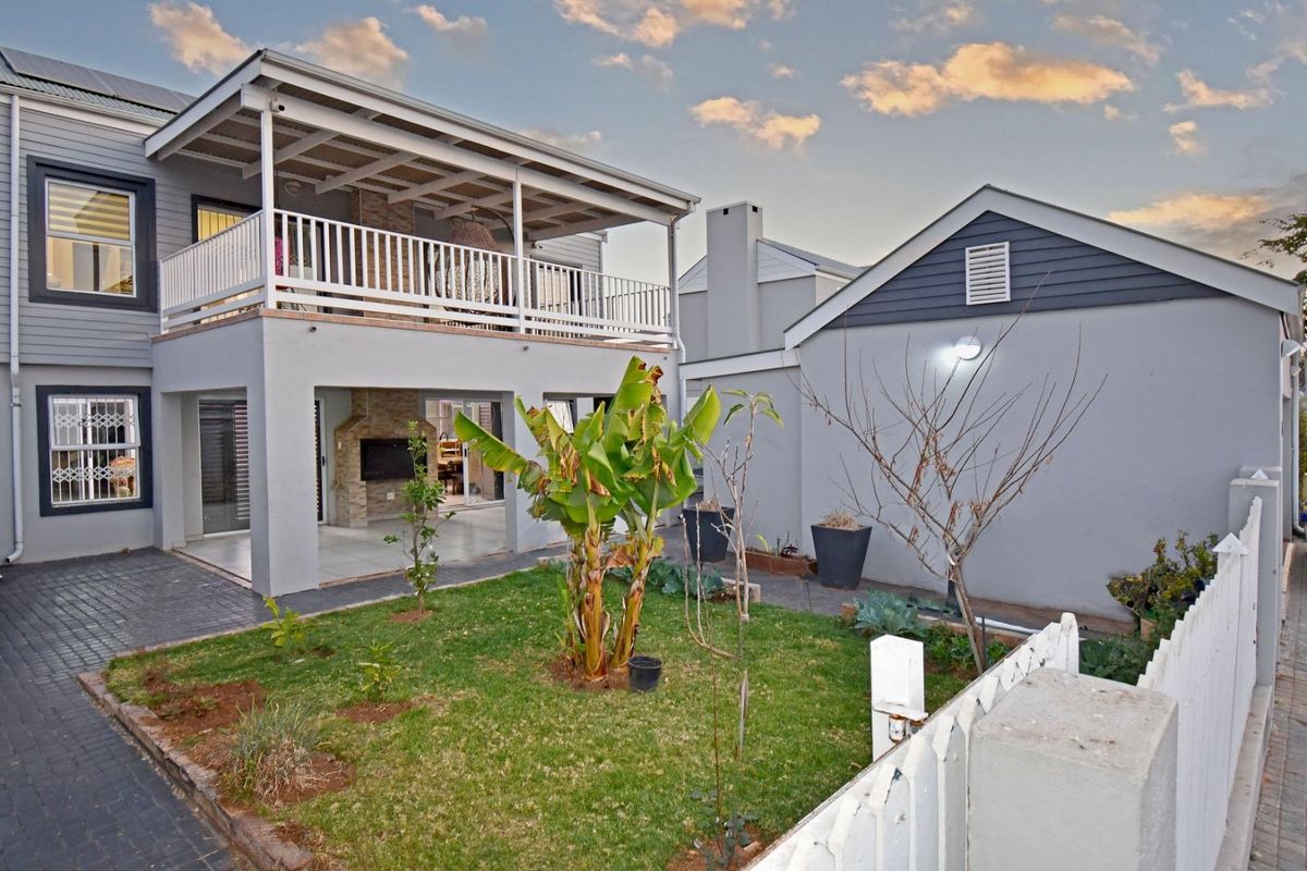 Rear view of the property featuring a covered patio with a built-in braai, an upper balcony, and a landscaped garden area.