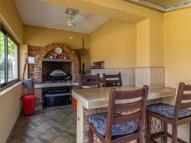 Covered outdoor patio area featuring a built-in brick braai, tiled breakfast bar, and ceiling fan, ideal for relaxed outdoor entertaining.