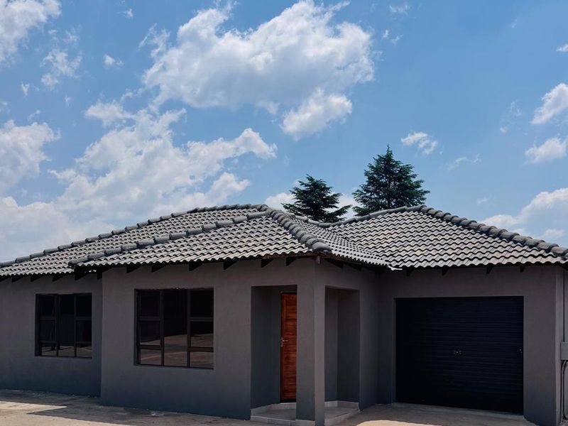 Front elevation of a modern townhouse featuring a dark grey facade, tiled roof, integrated garage, and a wooden entrance door.