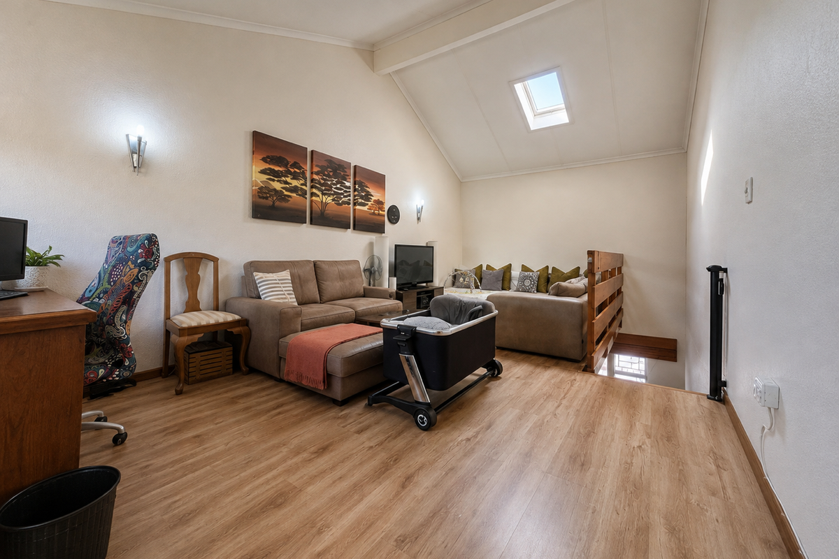 A spacious loft-style living area featuring vaulted ceilings, a skylight, and warm laminate flooring, creating a bright and inviting atmosphere.