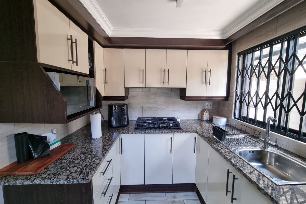 A well-maintained kitchen featuring granite countertops, built-in cabinetry, a gas hob, and a stainless steel sink with a security gate on the window.