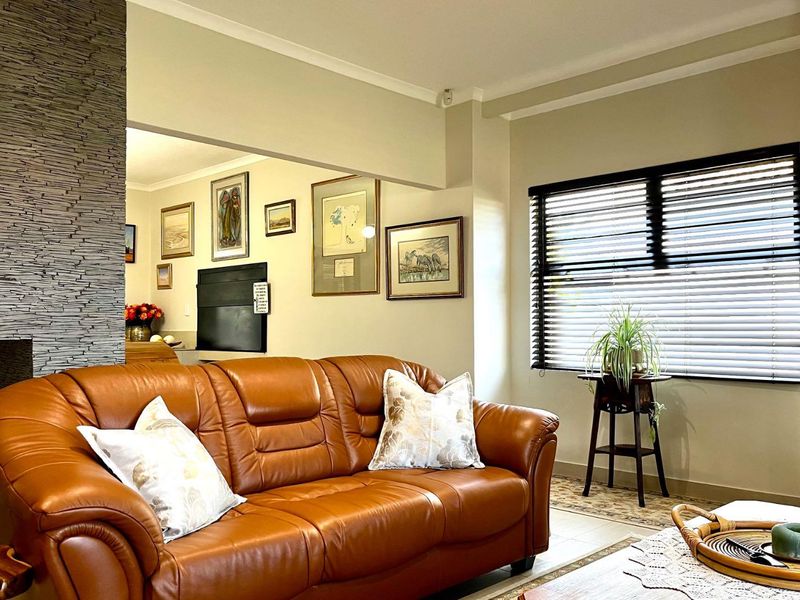 A comfortable living room featuring a textured stone accent wall and large windows with fitted venetian blinds, creating a warm and inviting atmosphere.