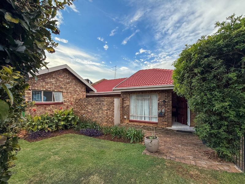 A well-maintained face brick house featuring a red tiled roof, a paved entrance walkway, and a neat front garden.