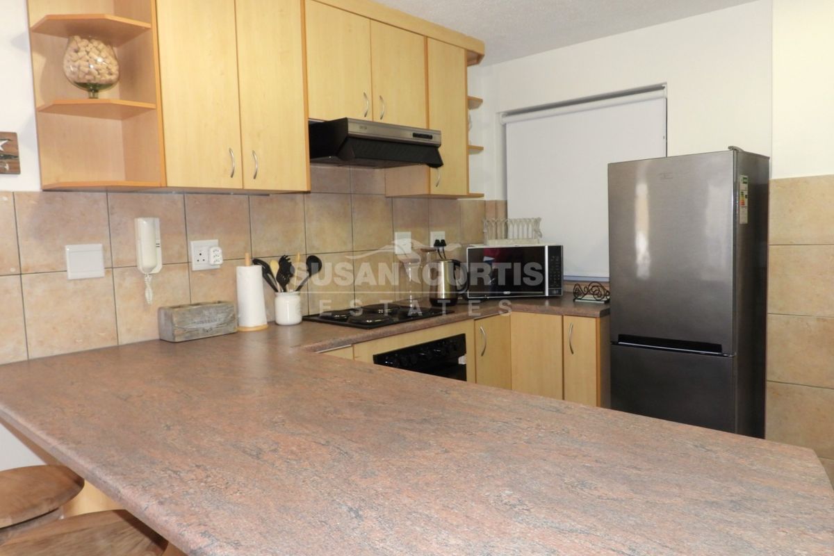 A functional kitchen featuring laminate countertops, tiled backsplash, built-in cabinetry, and integrated cooking appliances including a hob and extractor fan.