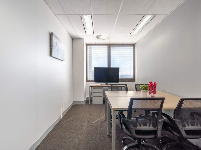 A functional office space featuring a suspended ceiling with recessed lighting, carpeted flooring, and large windows with blinds for natural light.