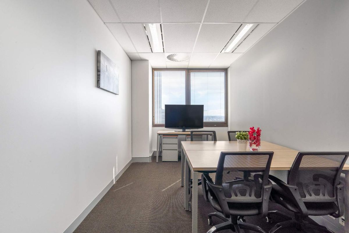 A functional office space featuring a suspended ceiling with recessed lighting, carpeted flooring, and large windows with blinds for natural light.