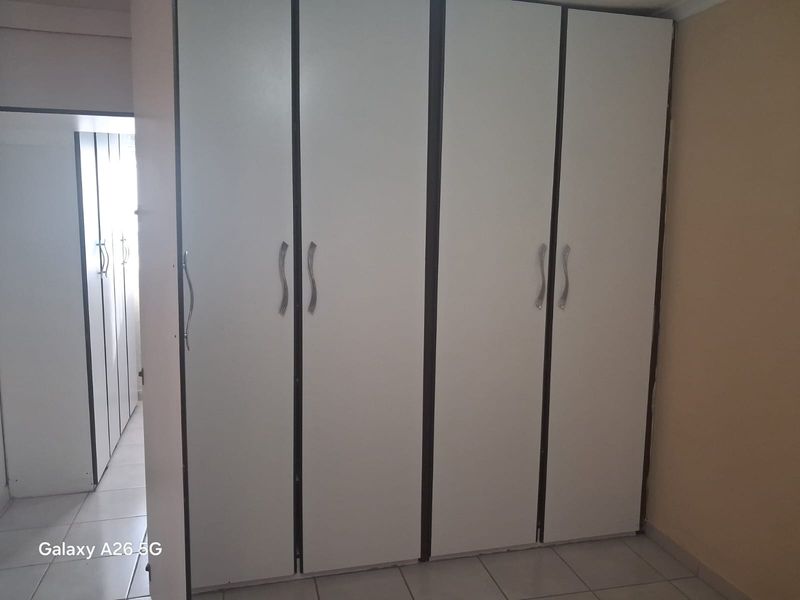A bedroom featuring white built-in cupboards and tiled flooring, offering ample storage space.
