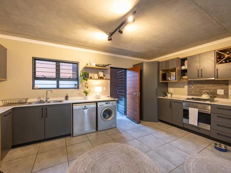 Modern kitchen featuring grey cabinetry, stone countertops, integrated gas hob, oven, and tiled flooring with direct access to an exterior area.