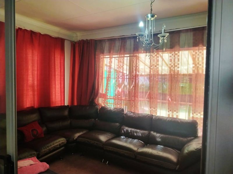 A living room featuring a chandelier, large windows with security bars, and access to an outdoor area through a sliding door.