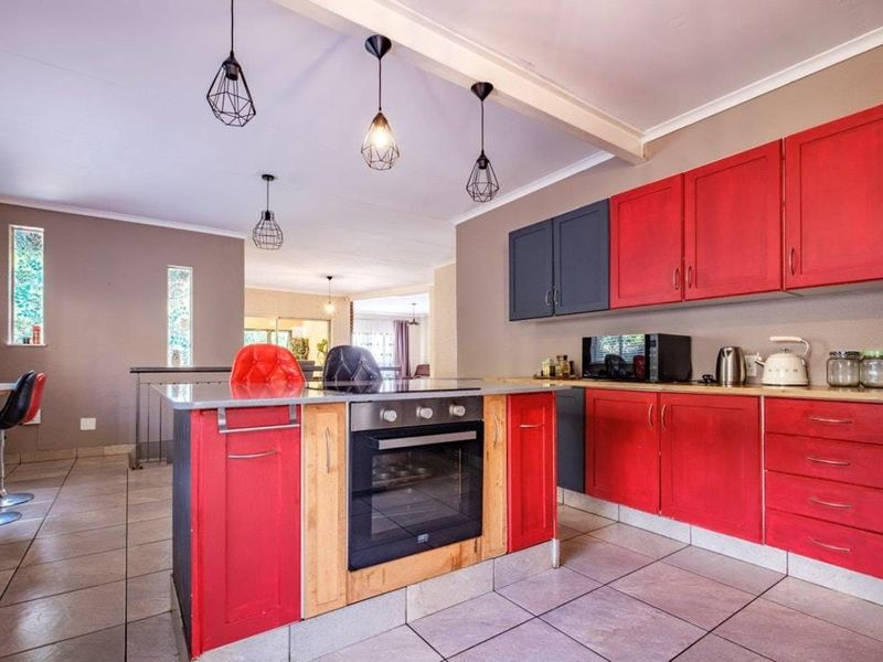 A vibrant kitchen featuring a central island with a built-in oven, contrasting red and dark grey cabinetry, and modern pendant lighting over tiled floors.