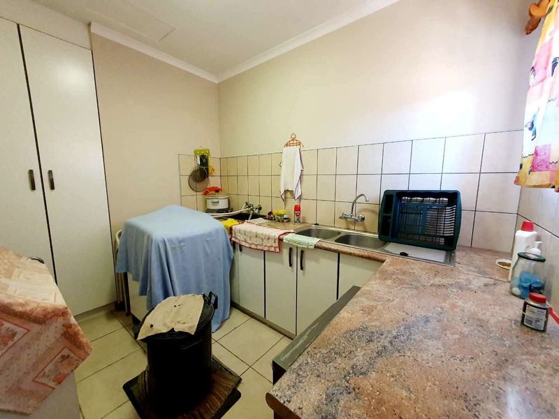 A functional laundry room featuring a double sink, tiled splashback, ample built-in cabinetry, and durable tiled flooring.