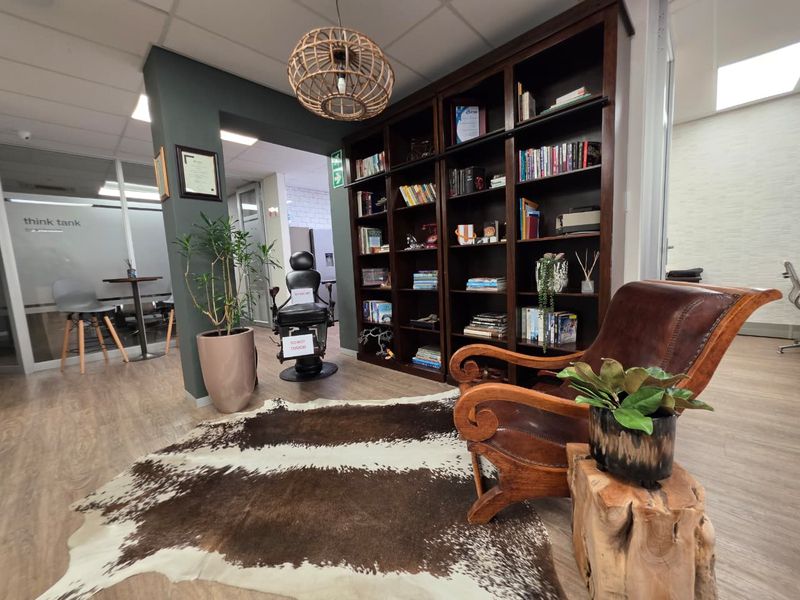 A professional office space featuring a large built-in wooden bookshelf, modern suspended ceiling, and glass partition walls creating a bright, functional work environment.