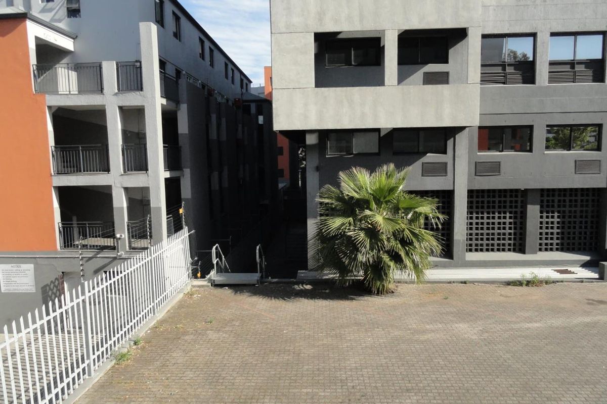 Exterior view of the apartment complex courtyard featuring paved ground, metal security fencing, and multi-story building facades.