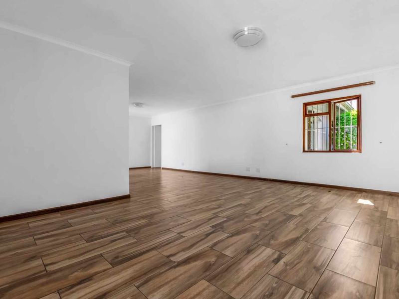 A spacious, vacant living area featuring modern wood-look tile flooring, crisp white walls, and a timber-framed window providing natural light.