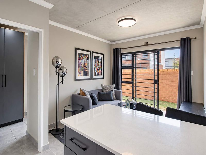 Modern open-plan living area featuring a sleek kitchen island with stone countertop, tiled floors, and sliding glass doors leading to a private outdoor space.