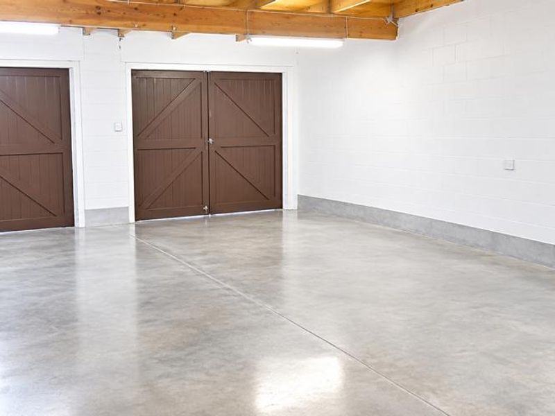 A clean, spacious double garage featuring polished concrete floors, exposed timber ceiling beams, and well-maintained painted blockwork walls.