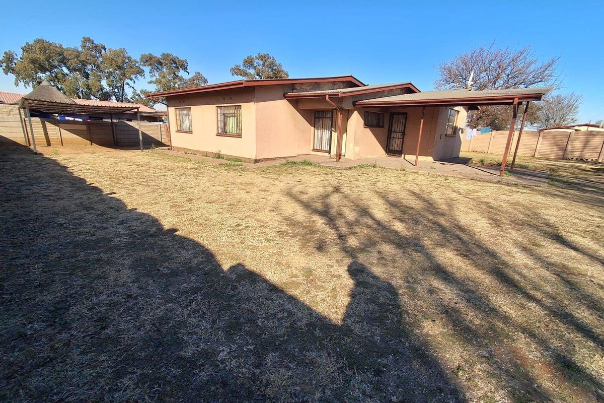 Rear view of the property featuring a covered patio, a detached thatched lapa, and a spacious backyard enclosed by perimeter walls.