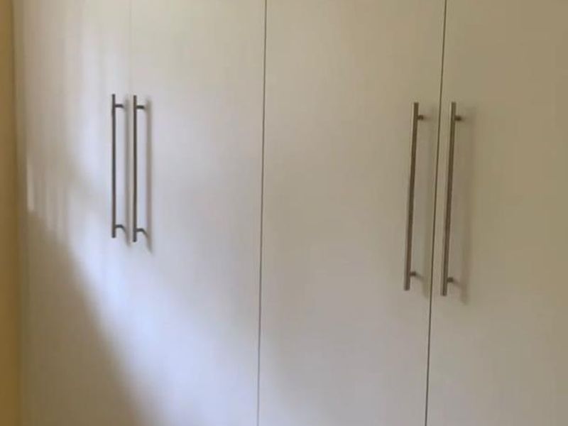 A bedroom featuring clean, white built-in cupboards with modern stainless steel handles, providing ample storage space.