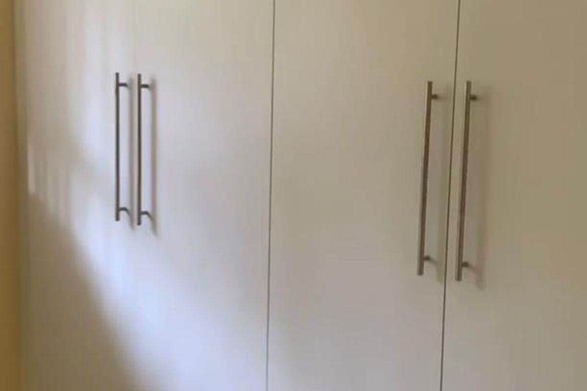 A bedroom featuring clean, white built-in cupboards with modern stainless steel handles, providing ample storage space.