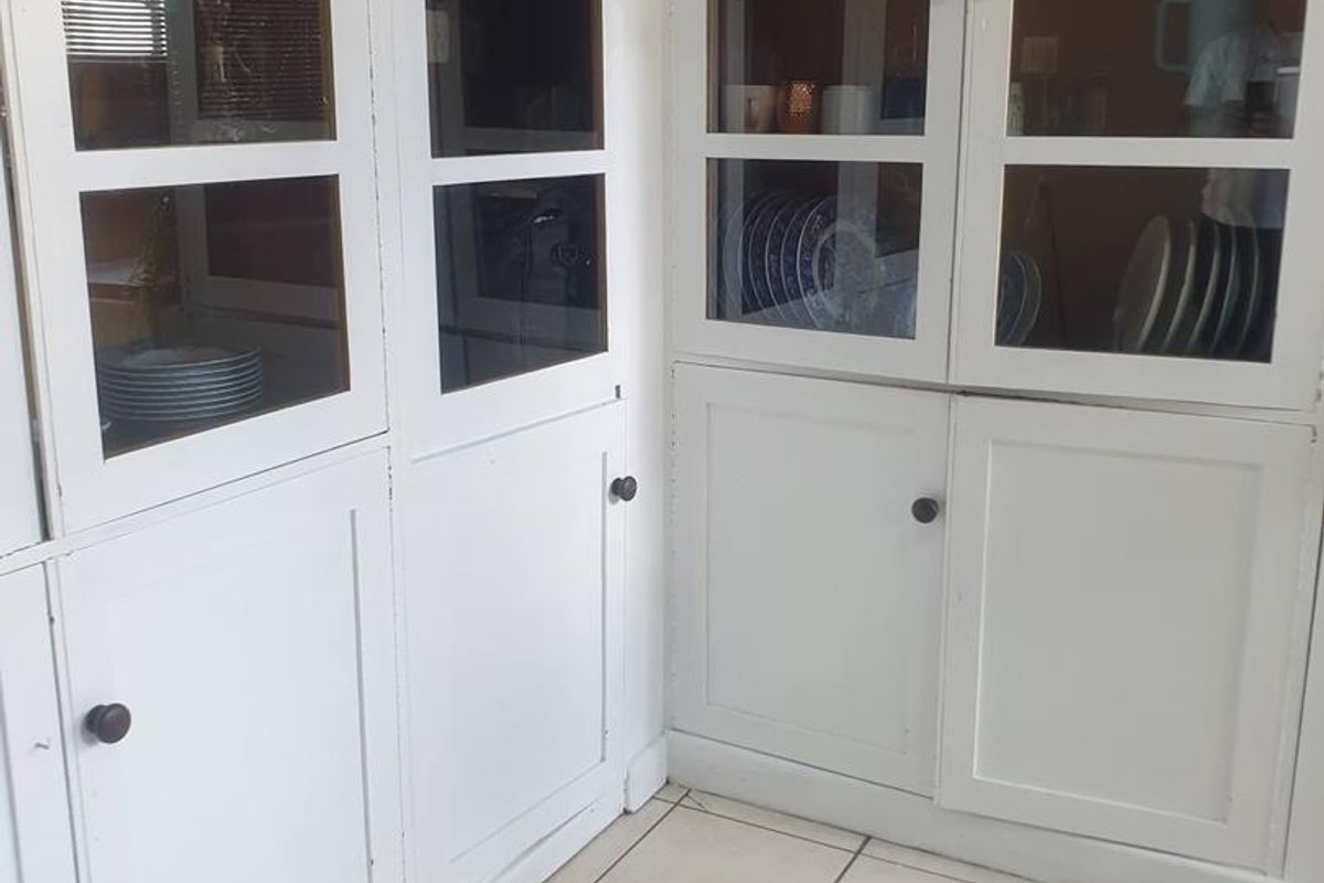 A corner view of a kitchen featuring white built-in cabinetry with glass-fronted upper doors and tiled flooring.