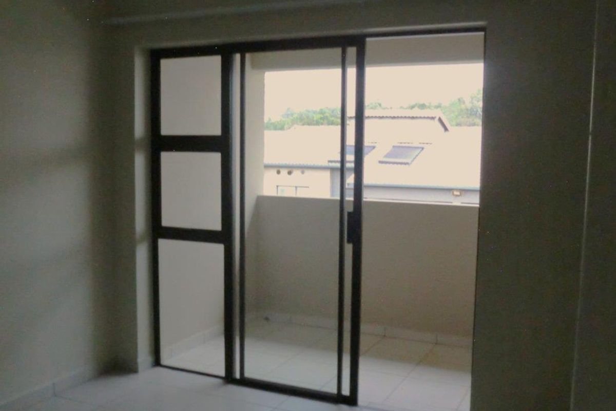 An empty living area featuring tiled flooring and large sliding glass doors that open onto a private balcony.