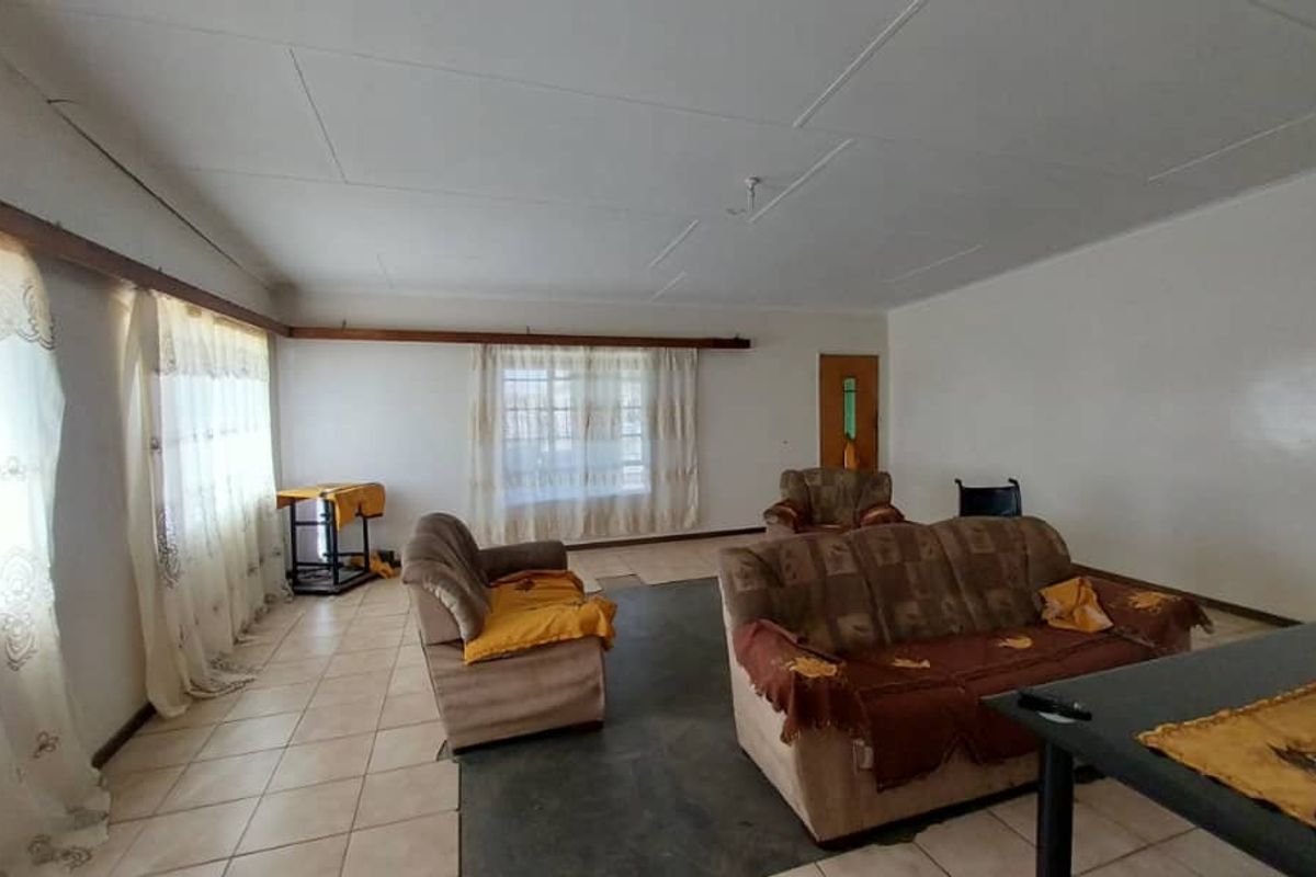 A spacious living room featuring tiled flooring, large windows with natural light, and a neutral interior finish.