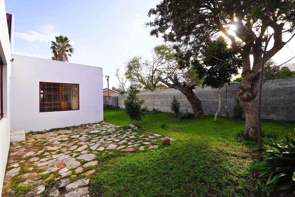 A rear garden area featuring a stone-paved patio, established trees, and a concrete block boundary wall.