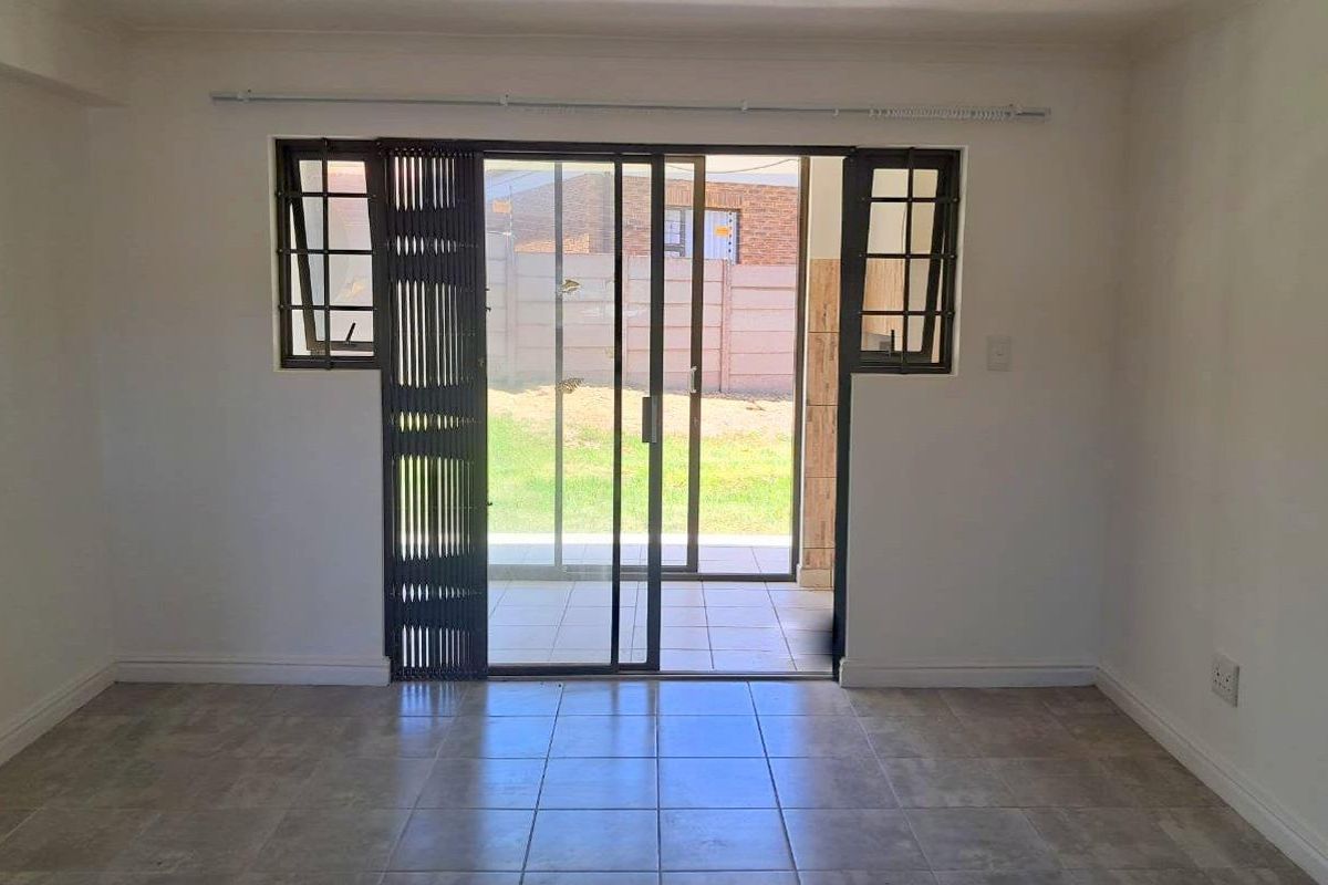 A bright, empty living room featuring tiled flooring and a sliding glass door that provides direct access to the outdoor patio area.