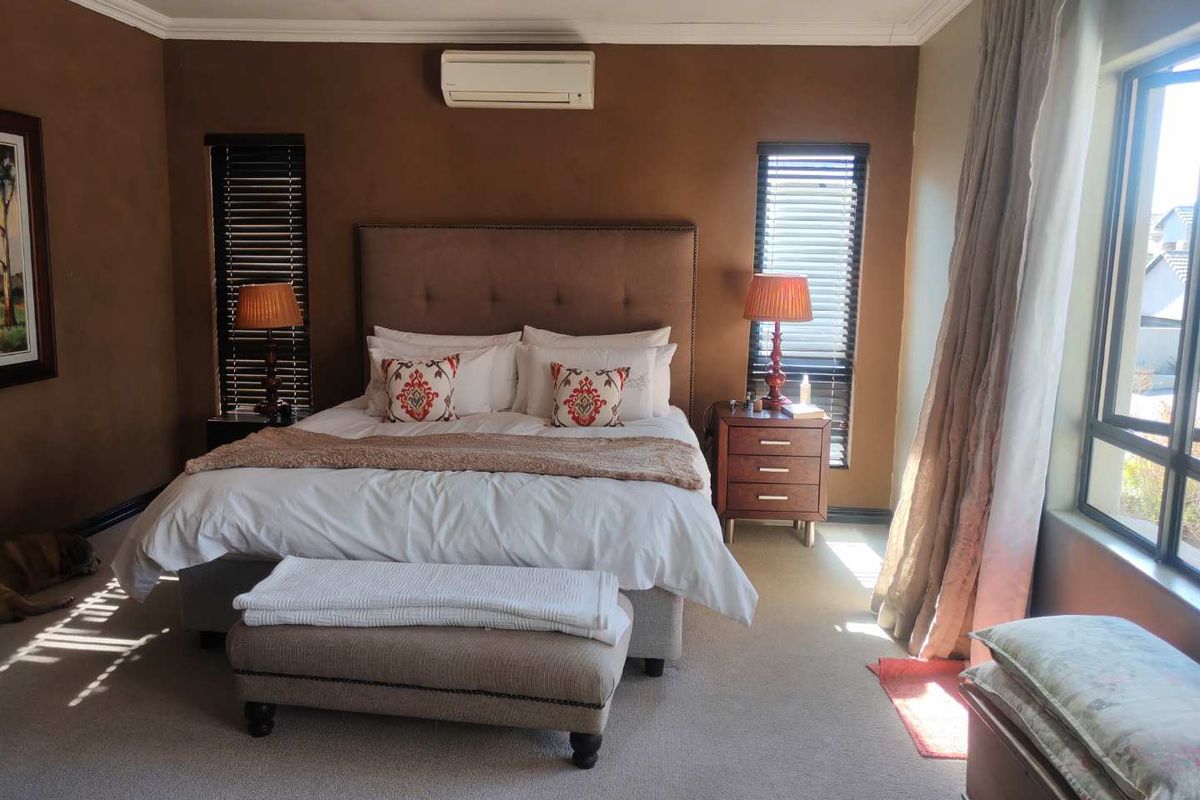Spacious bedroom featuring neutral carpet flooring, a wall-mounted air conditioning unit, and dual windows with fitted venetian blinds.